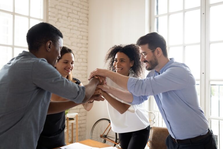Four millennial different ethnicity teammates stacked palms together feels unity and support. Celebrating profitable deal, common success, leadership in market, participating in team building concept