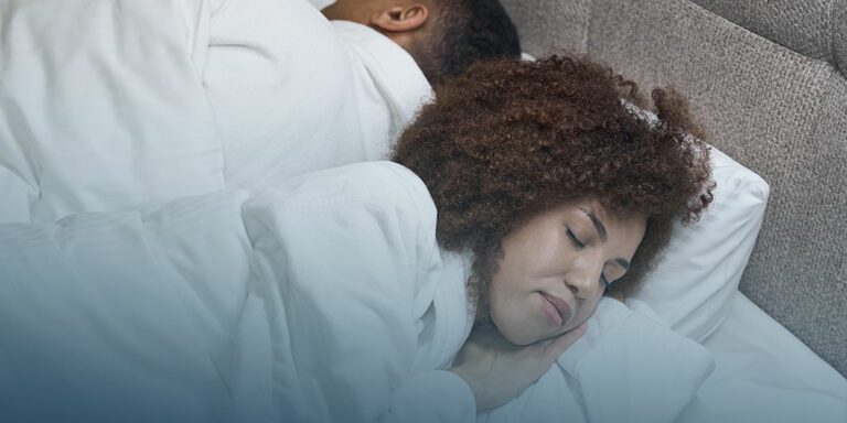 woman with dark skin and curly hair in white pajamas sleeps on a bed with white bedding to unlock the power of sleep and relaxation