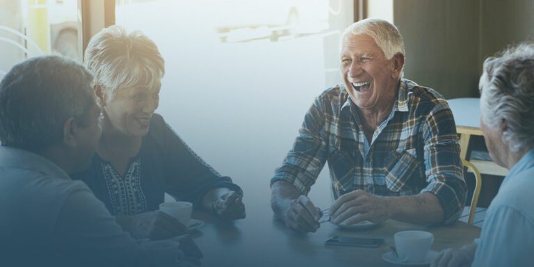 group of older adults sit around a table drinking coffee, smiling and laughing as they embody how social connections promote healthy aging and mental health