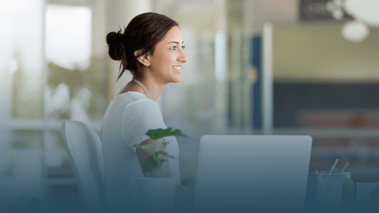 smiling woman sits at a desk with a laptop learning five strategies to support behavioral health for a healthier workforce