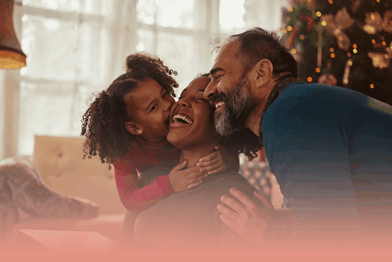 family exchanges embraces in front of the Christmas tree while celebrating with intention this holiday season.