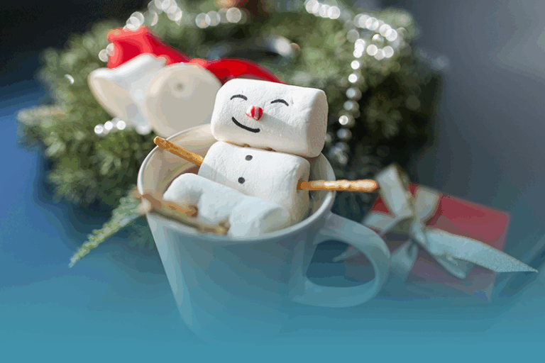 a marshmallow decorated to look like a little snowman relaxes in a mug of hot chocolate representing National Stress-Free Holidays Month.