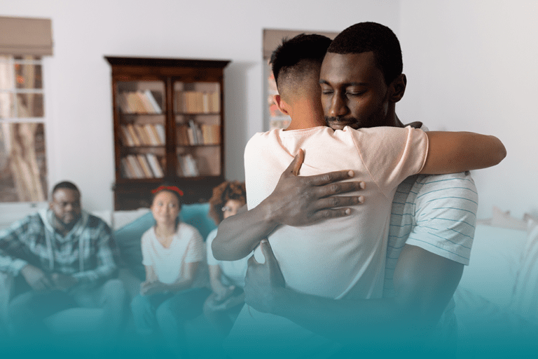 two men embrace while friends and family look on demonstrating they are supporting a loved one's mental health
