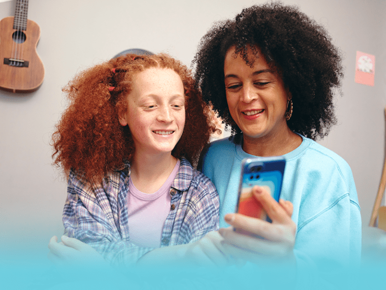mother and daughter look at phone as mom spends time teaching kids digital health literacy.