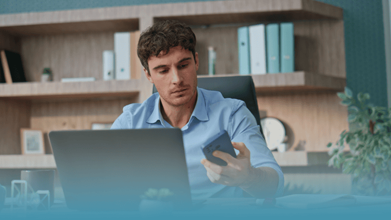 man working at laptop checks phone distractedly demonstrating caregiving as a workforce issue